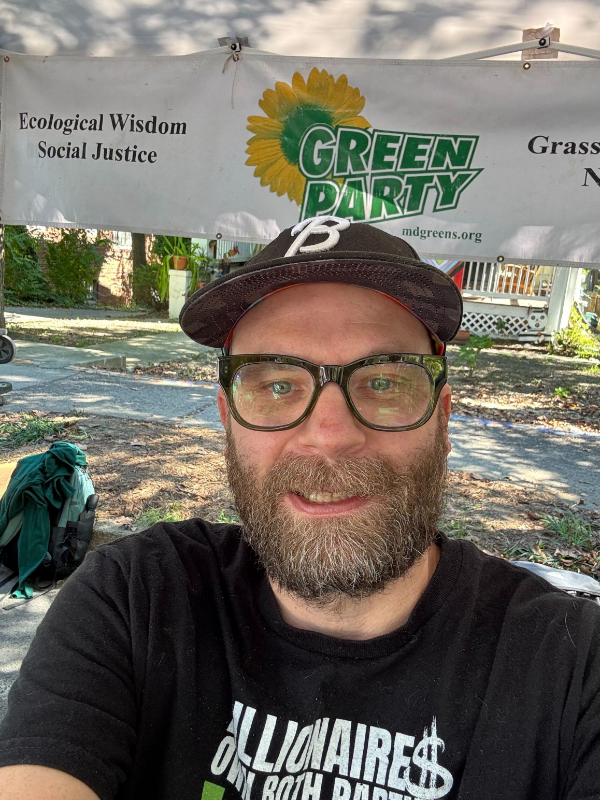 Andy smiling in front of a Green Party banner.